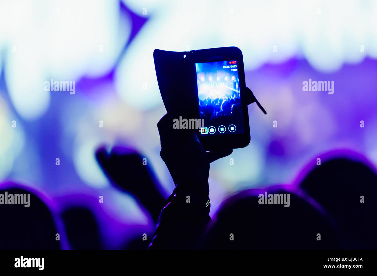 A member of the audience video records a performance at a music concert using their smartphones. Stock Photo