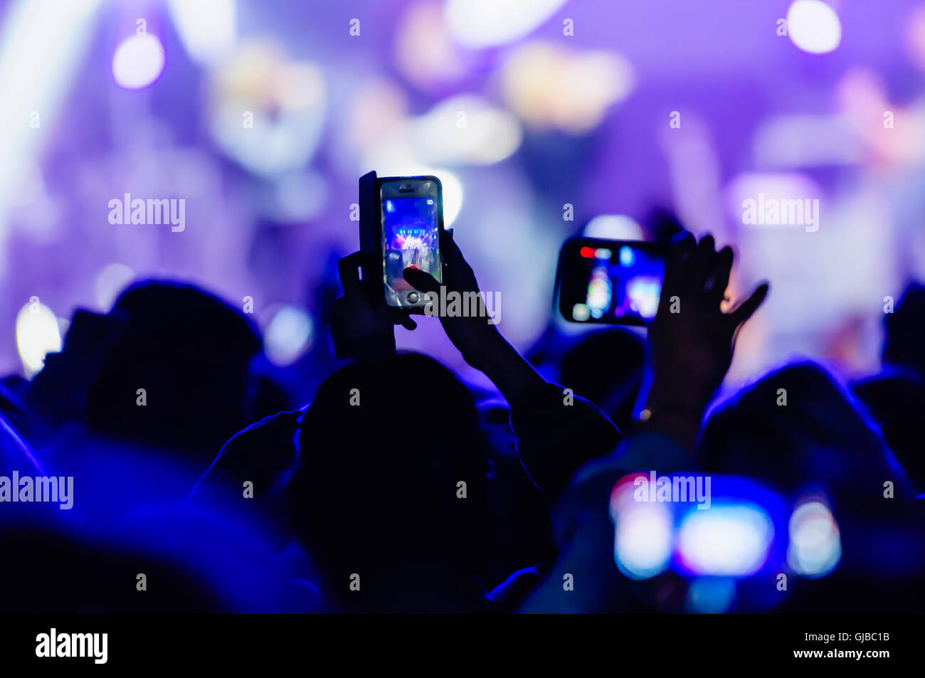 Members of the audience video record a performance at a music concert using their smartphones. Stock Photo