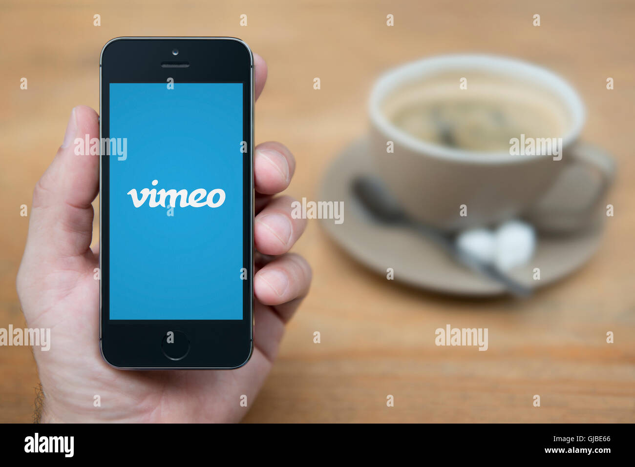 A man looks at his iPhone which displays the Vimeo logo, while sat with a cup of coffee (Editorial use only). Stock Photo