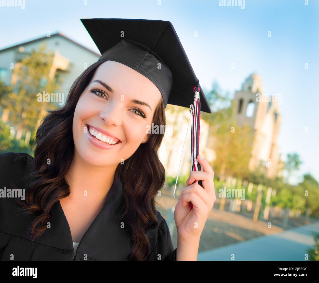 Happy Graduating Mixed Race Woman In Black Cap and Gown Celebrating on Campus. Stock Photo