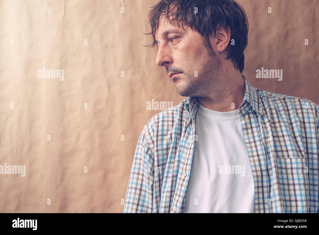 Depressive sad man profile portrait, male person with unhappy gloomy facial expression leaning on to wall and looking to a side. Stock Photo