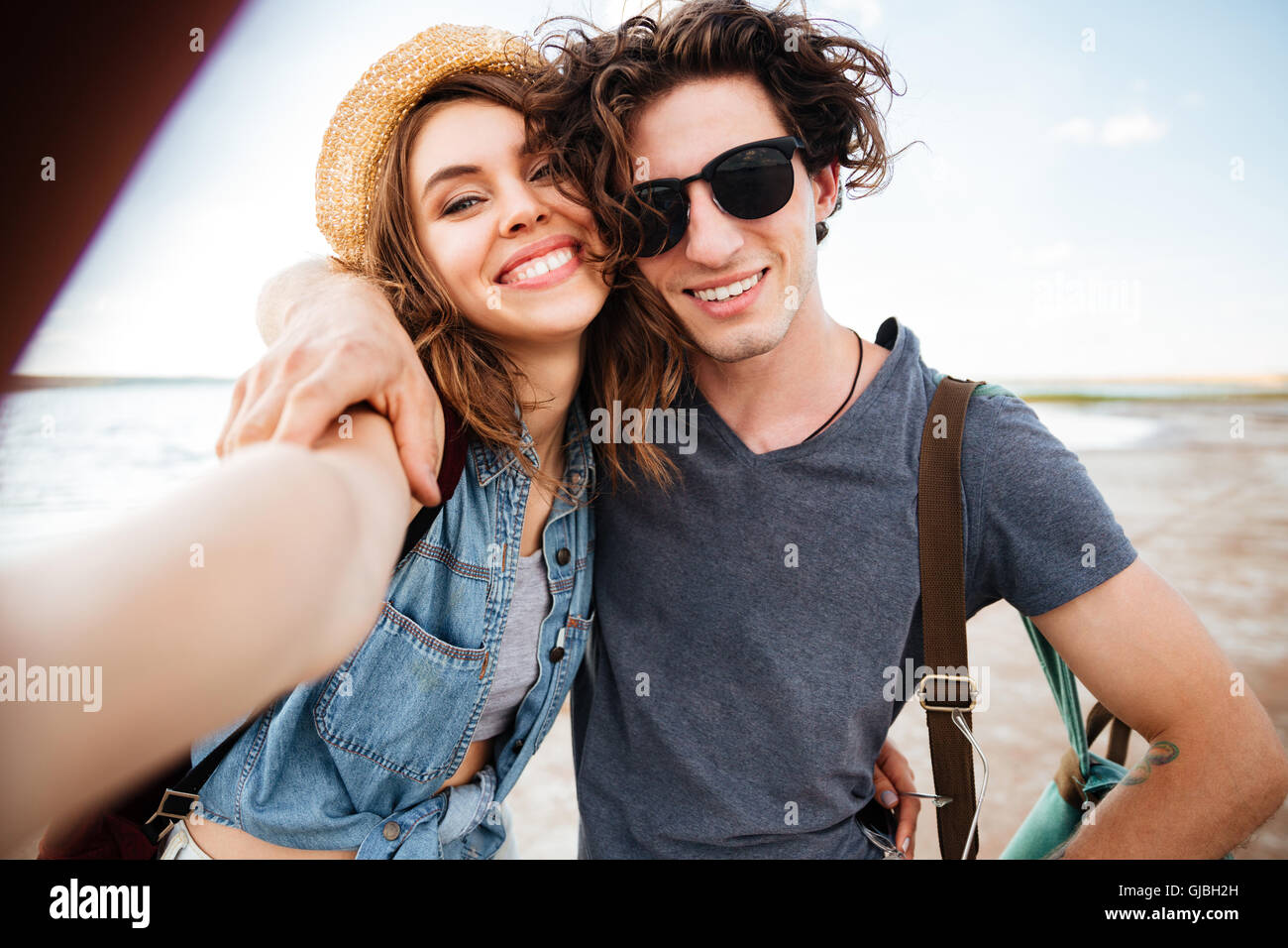 Smiling beautiful young couple hugging and taking selfie on the beach Stock Photo