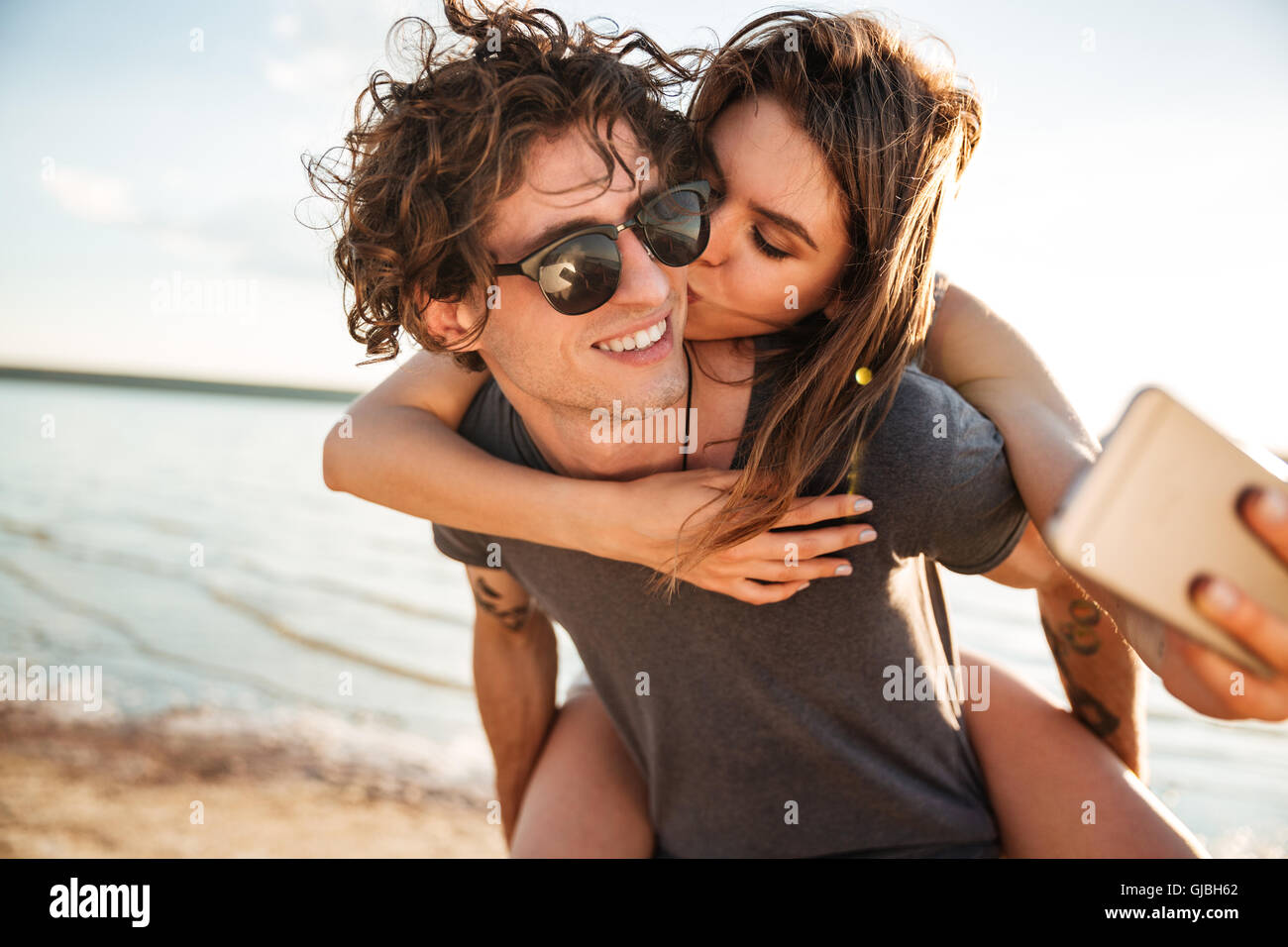 Young happy couple in love kissing and making selfie at the beach, piggyback ride Stock Photo
