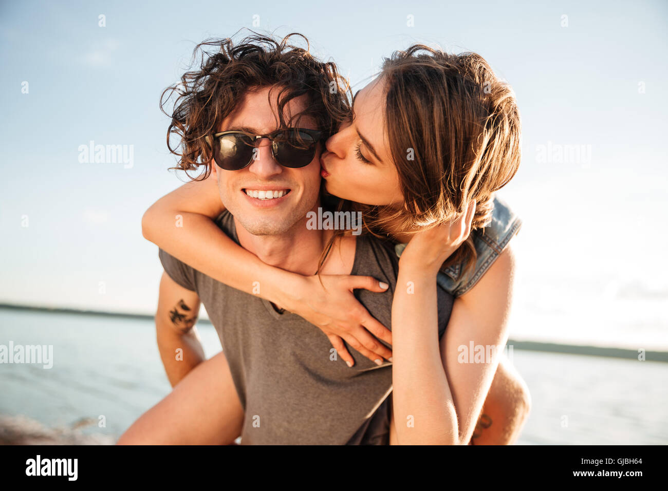Young man giving piggyback ride to girlfriend by the ocean Stock Photo