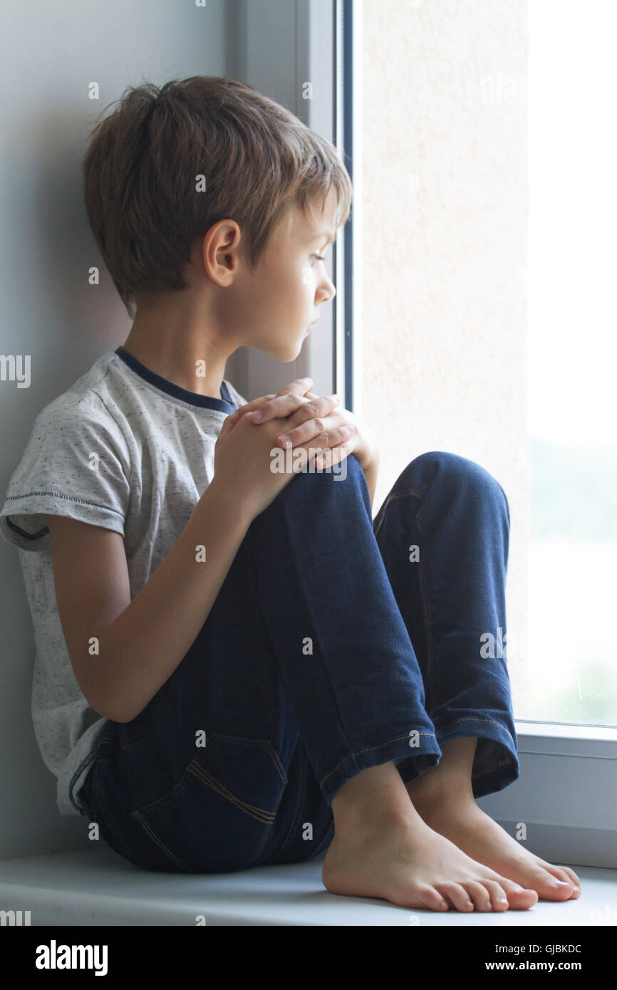 Sad lonely child sitting alone on the window at home Stock Photo