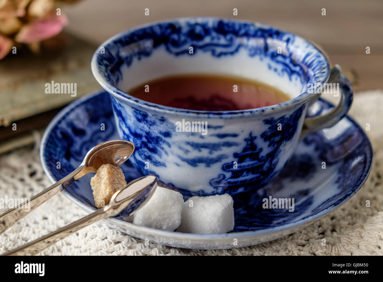 Cup of tea in antique blue and white china cup and saucer with brown and white sugar cubes, sugar tongs with lace cloth Stock Photo