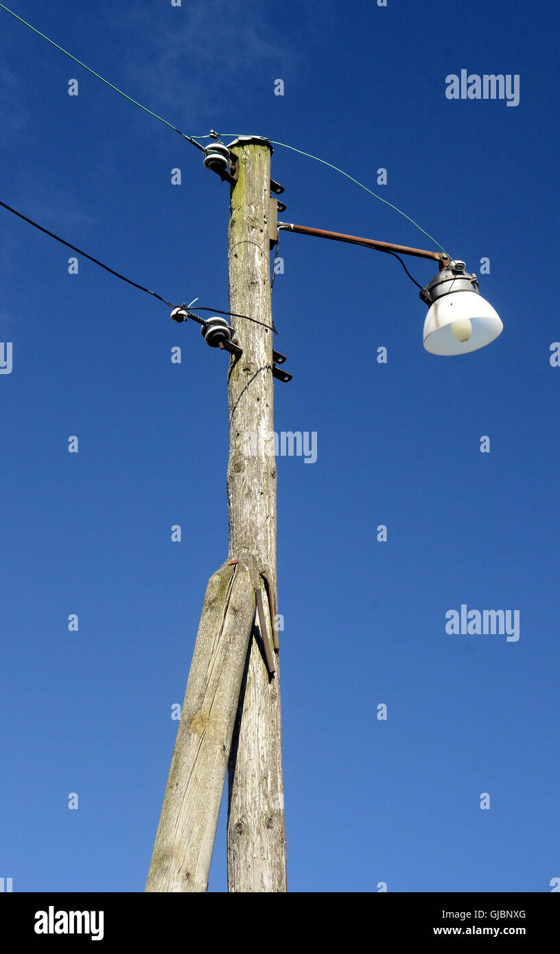 Old wooden lamp post with light bulb and overhead wires. They use steel, cables and LED lights now. Stock Photo