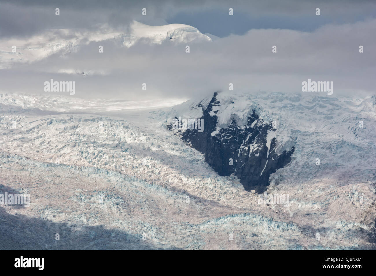 The wall of ice that is Kennicott Glacier flows around a large rock cliff face. Stock Photo