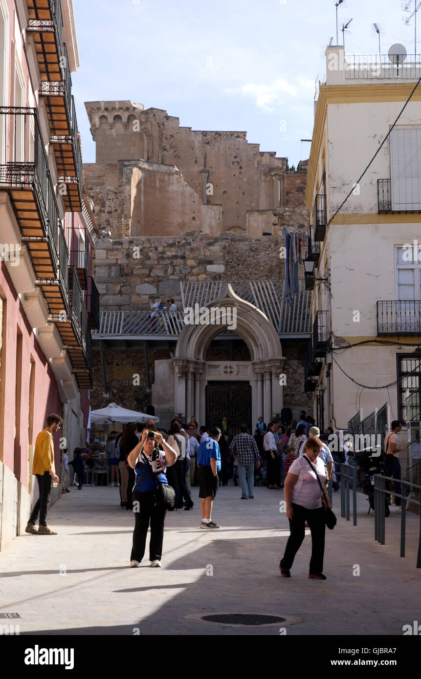 Tourist wander by modern buildings, ancient Roman theater ruins rise up behind the buildings. Stock Photo