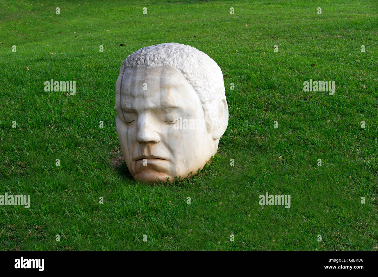White marble head of roman ruin statue sits in grass near the town hall. Stock Photo
