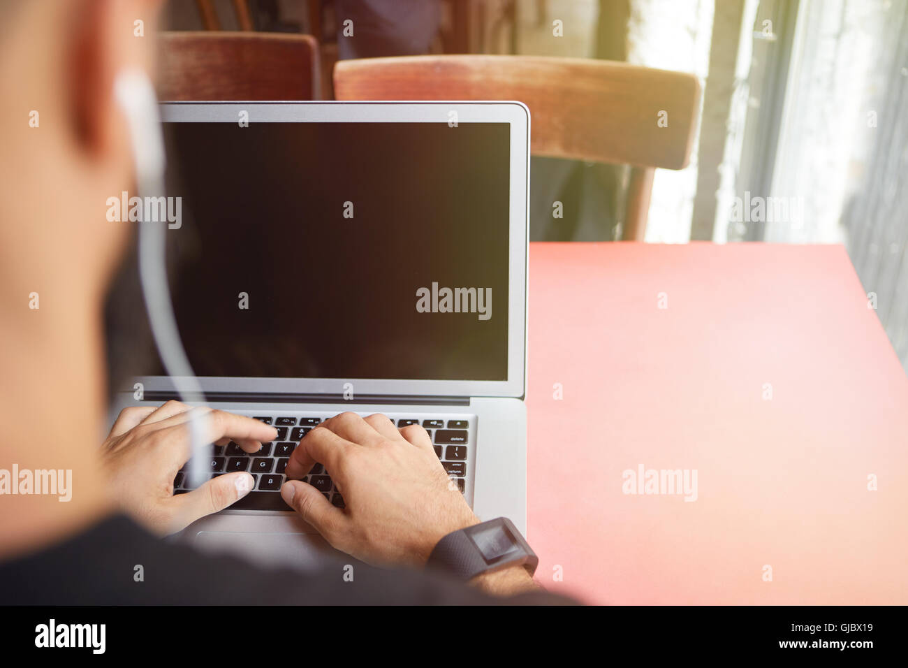 Young Bearded Businessman Wearing Black Tshirt Working Laptop Urban Cafe.Man Sitting Wood Table Headphones Using Notebook Empty Screen.Coworking Process Business Startup.Blurred Background Stock Photo