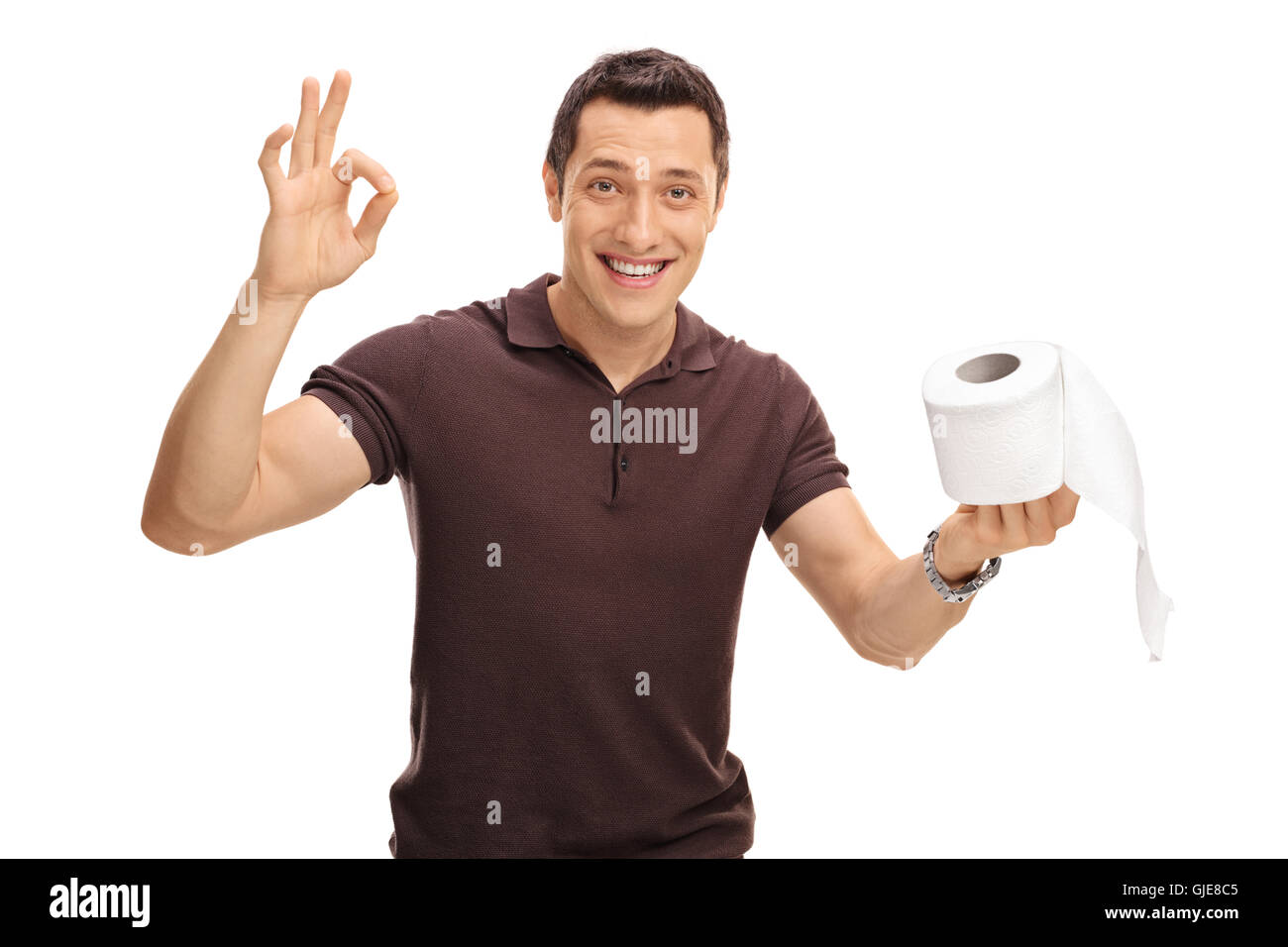 Smiling young man holding a toilet paper roll in one hand and making an ok gesture with his other isolated on white background Stock Photo