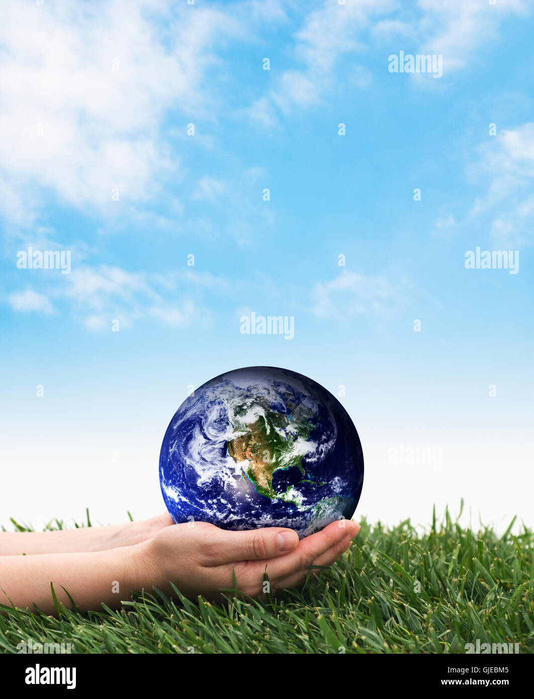 Hands holding earth over grass on a blue sky.  The planet earth image provided by NASA  http://www.earthobservatory.nasa.gov Stock Photo