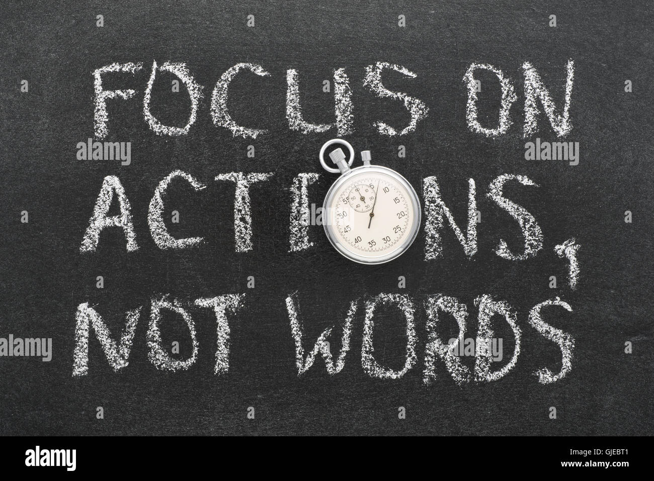 focus on actions, not words phrase handwritten on chalkboard with vintage precise stopwatch used instead of O Stock Photo