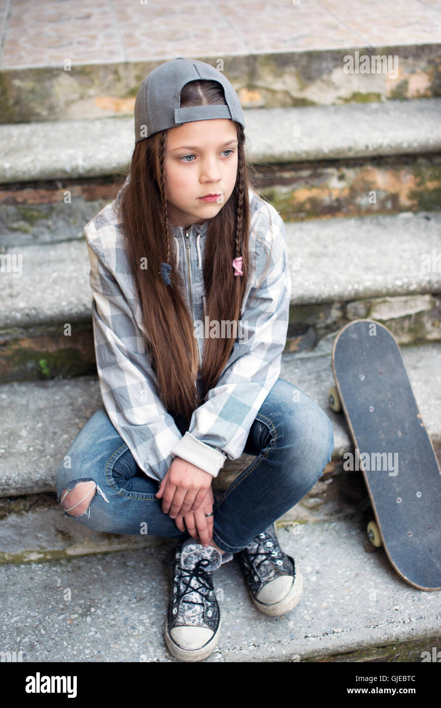 child girl sit on concrete stairs with skateboard Stock Photo