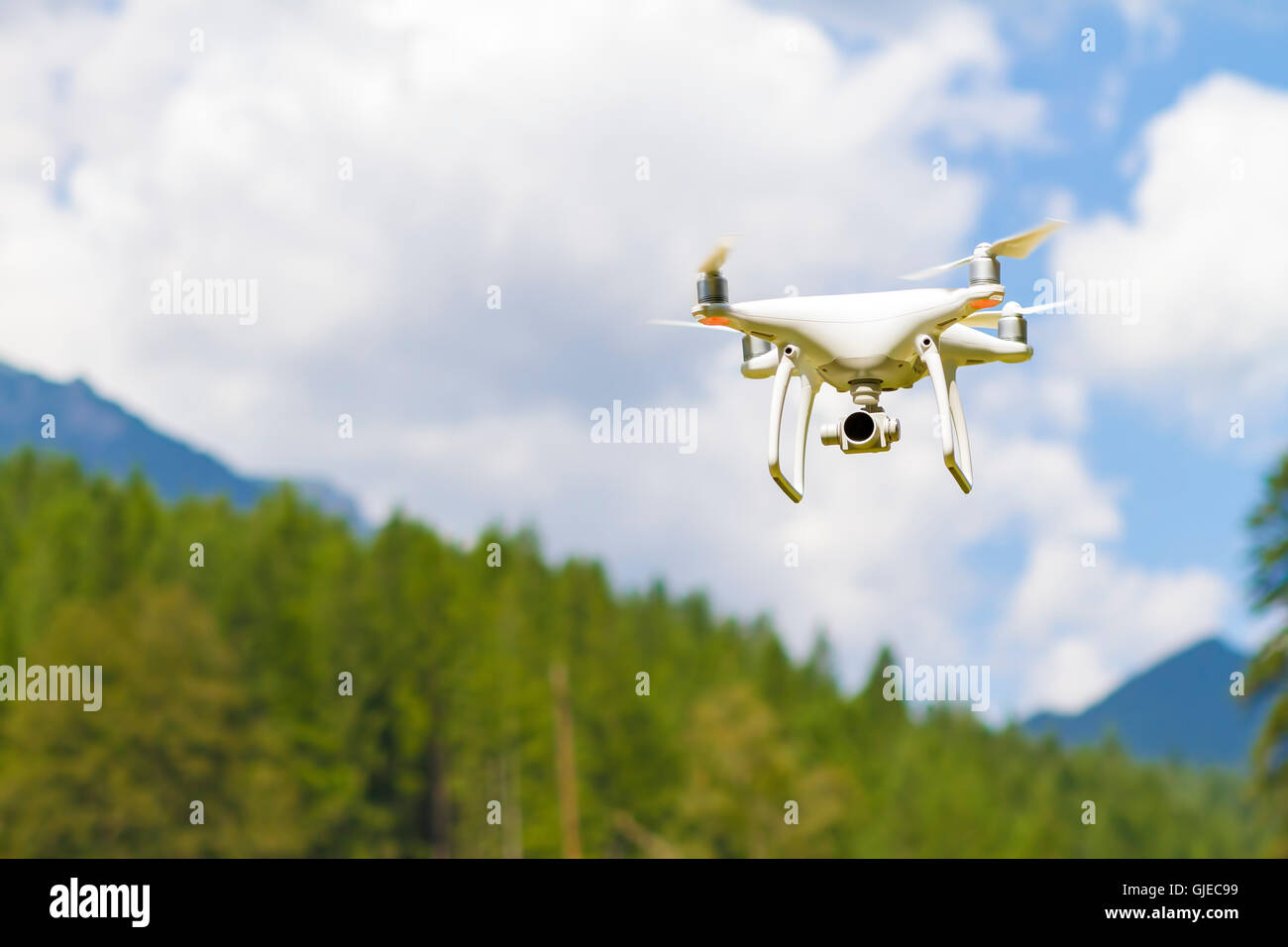 White drone quad copter with high resolution digital camera flying in the blue sky over the mountain Stock Photo