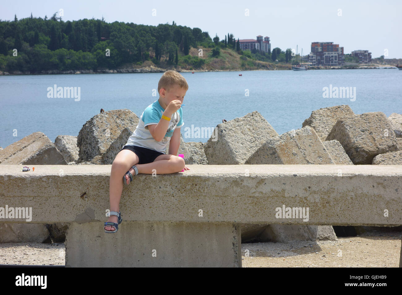 Boy sitting by the sea on a concrete fence and blow bubbles Stock Photo