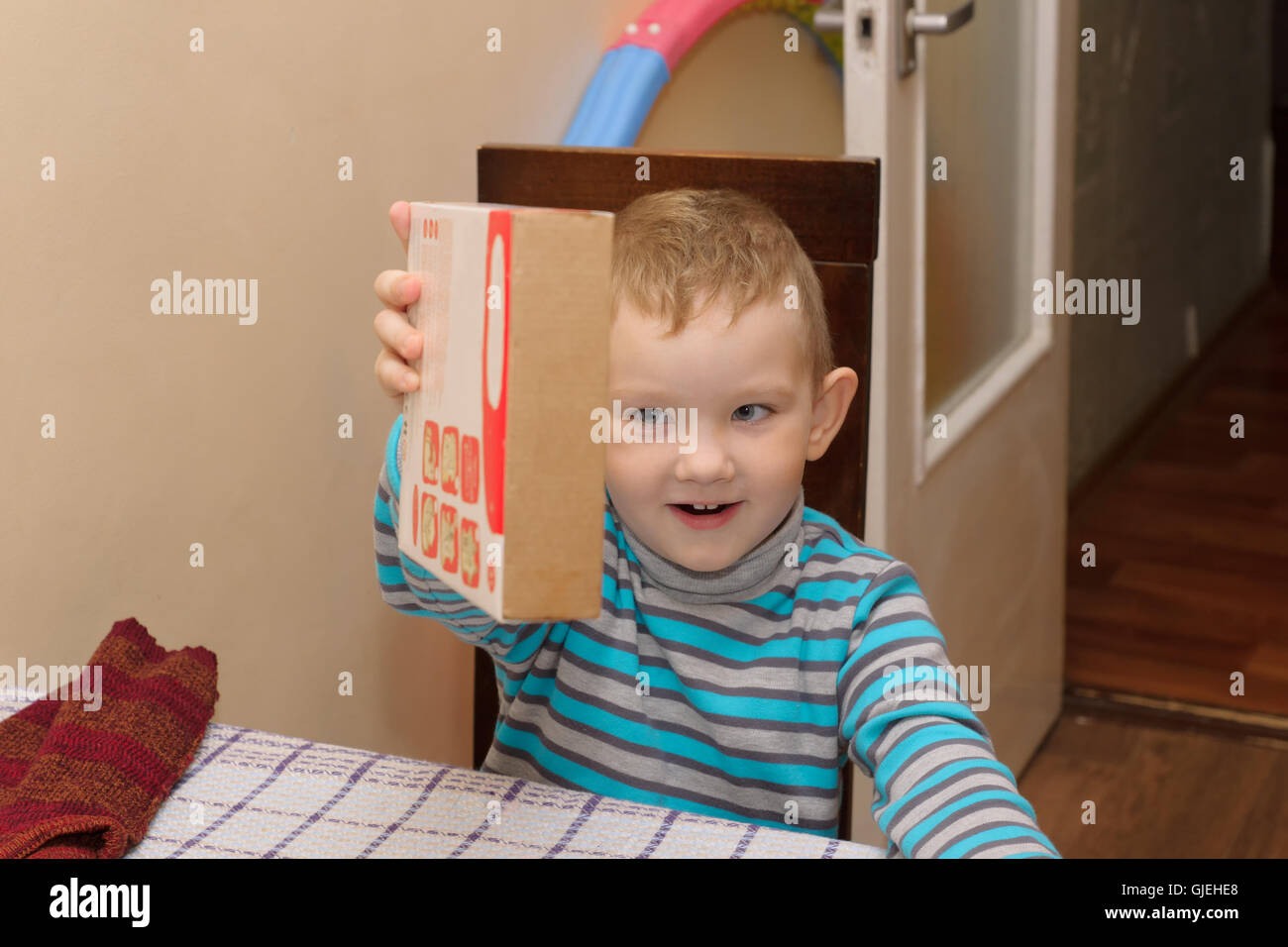 boy sitting at a table with a cardboard box in which lies a wooden constructor Stock Photo