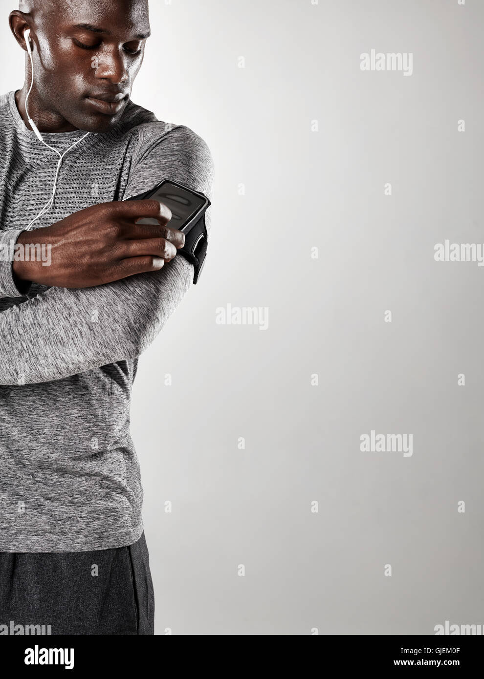 Shot of young black male model listening to music on cell phone. Man with mobile phone armband standing against grey background Stock Photo
