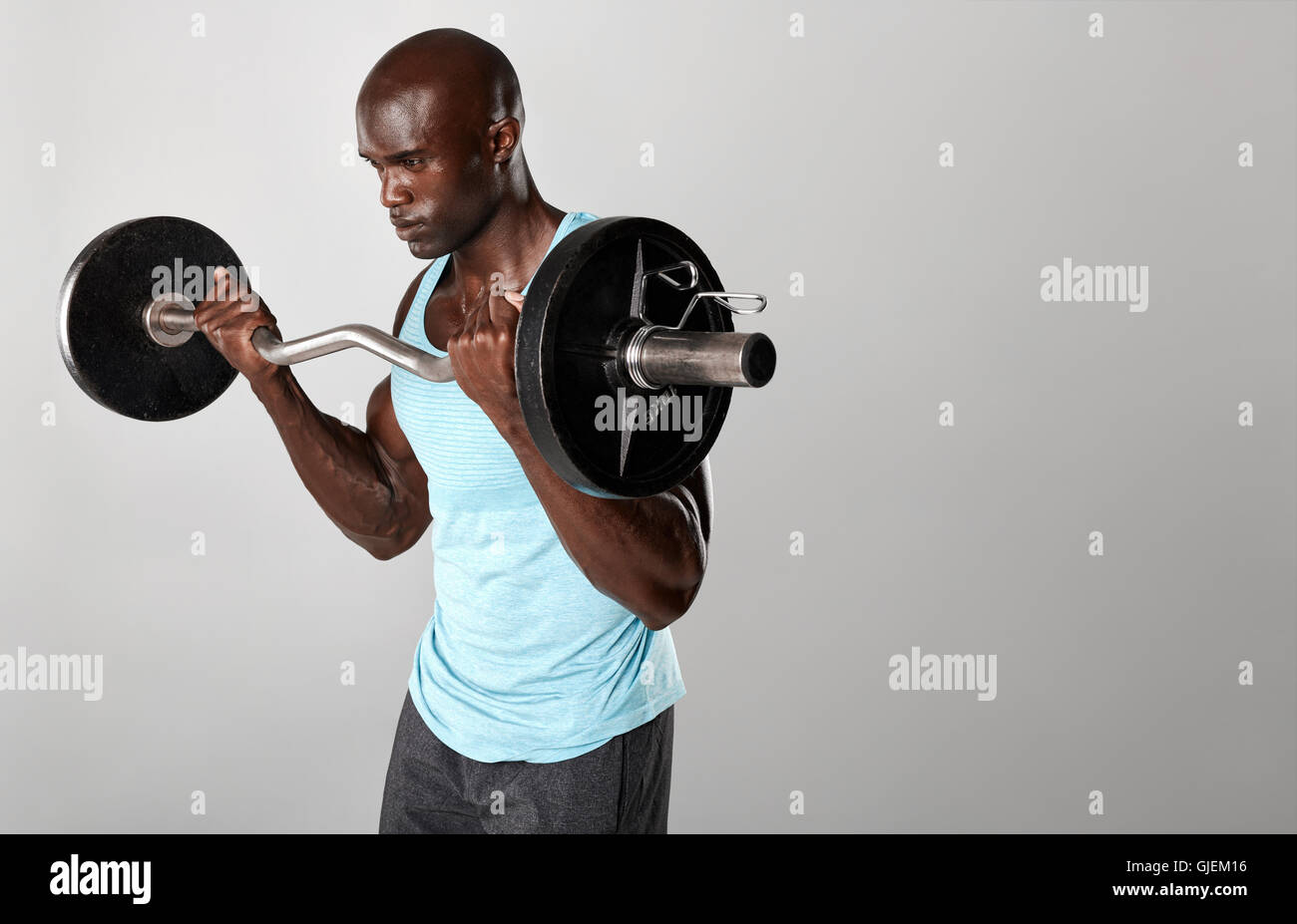 Portrait of young fit man lifting barbell against grey background. Young muscular man exercising with weights. Stock Photo