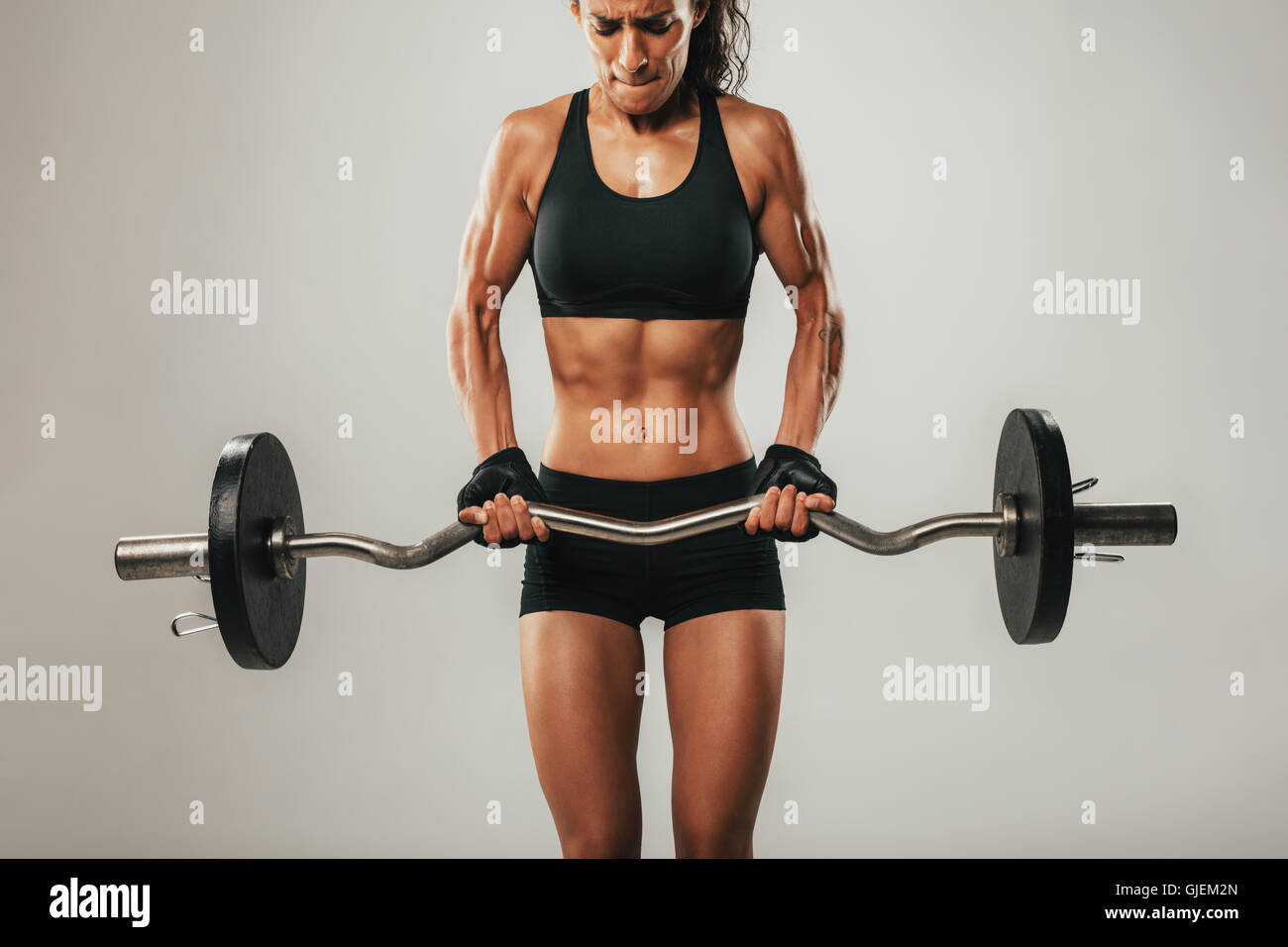 Muscles buldging on arms of muscular young woman using barbell weight Stock Photo