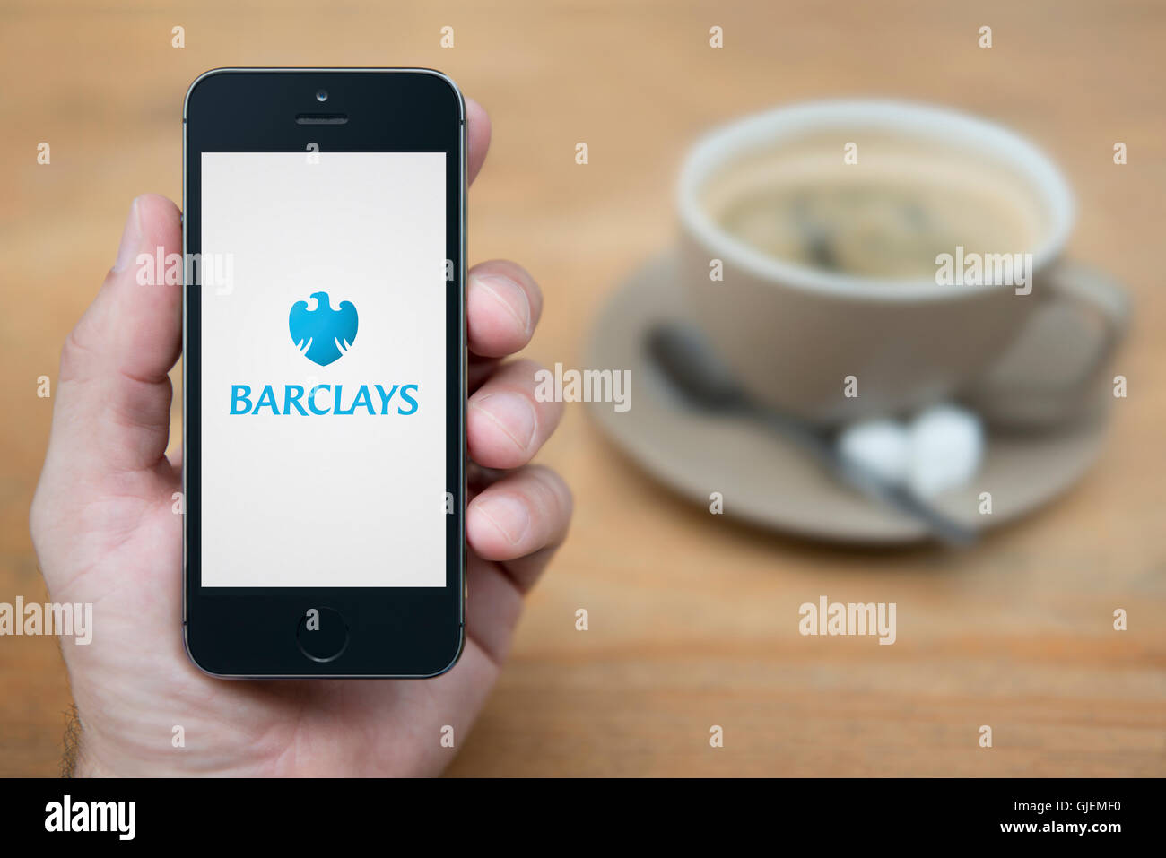 A man looks at his iPhone which displays the Barclays bank logo, while sat with a cup of coffee (Editorial use only). Stock Photo