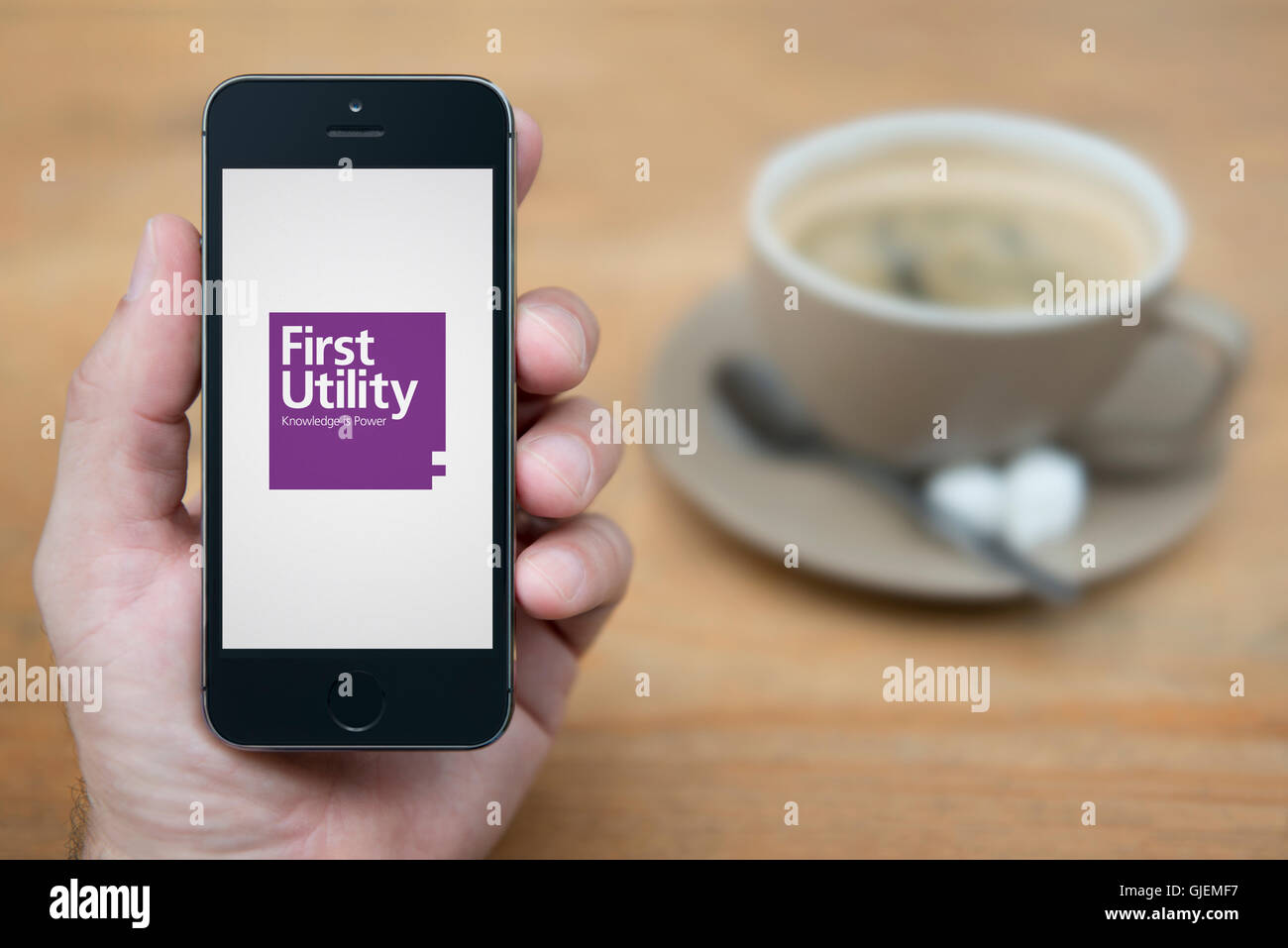 A man looks at his iPhone which displays the First Utility logo, while sat with a cup of coffee (Editorial use only). Stock Photo