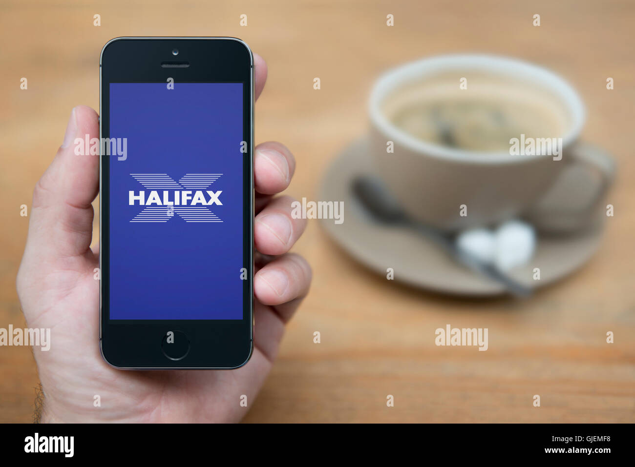 A man looks at his iPhone which displays the Halifax bank logo, while sat with a cup of coffee (Editorial use only). Stock Photo