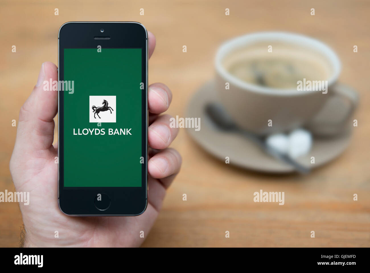 A man looks at his iPhone which displays the Lloyds bank logo, while sat with a cup of coffee (Editorial use only). Stock Photo