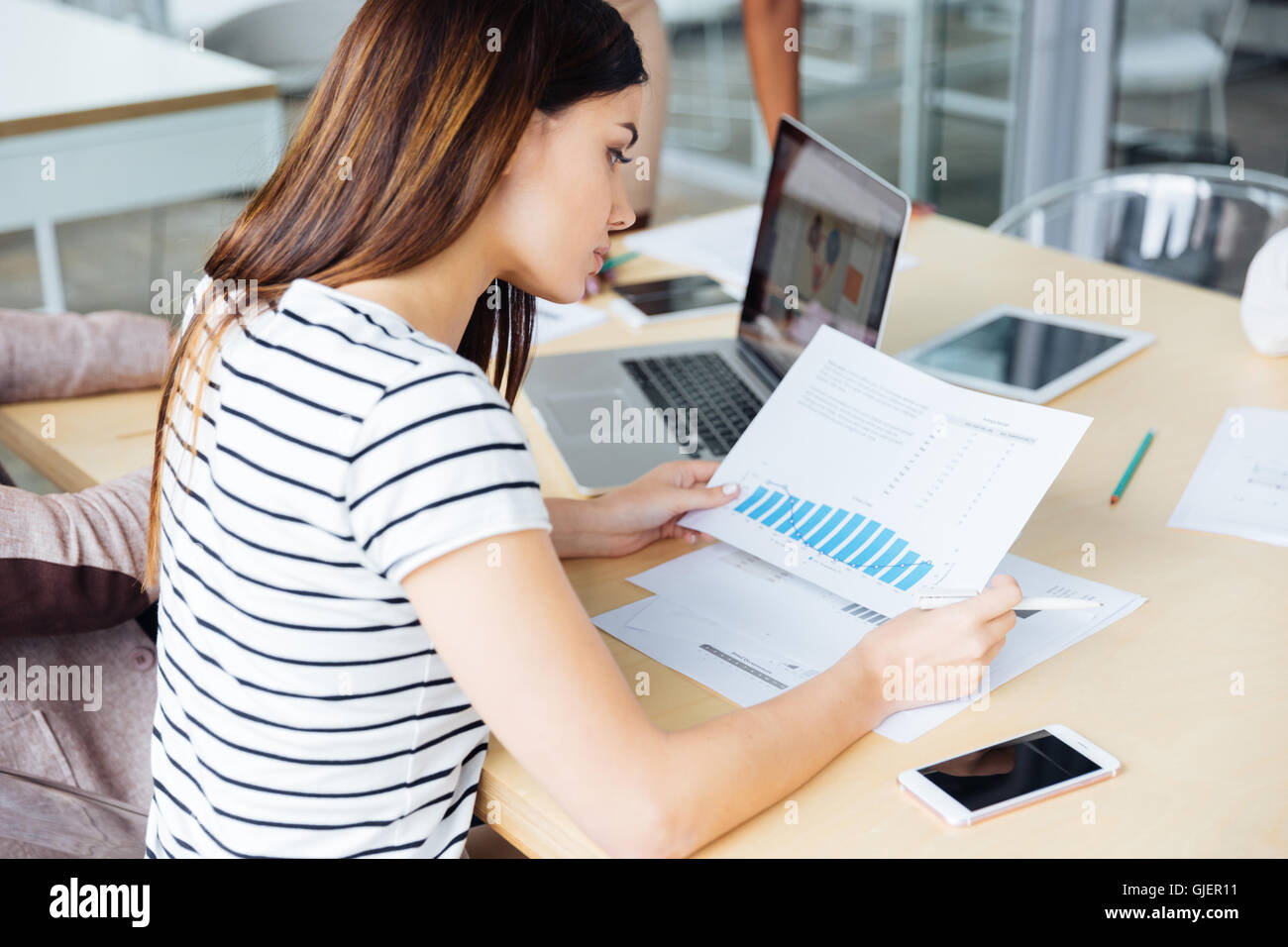 Thoughtful pretty young woman sitting and working on business meeting in office Stock Photo