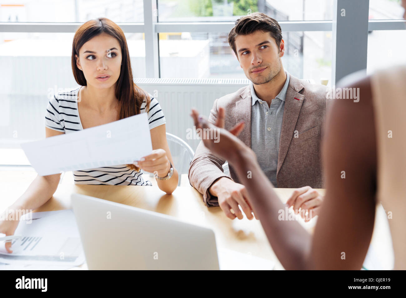 Three concentrated young businesspeople working with documents and using computer in office together Stock Photo