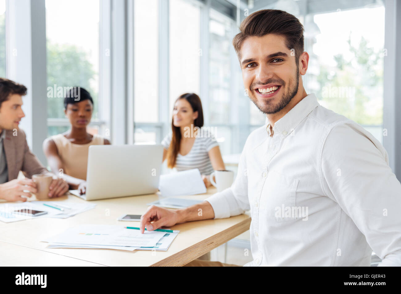 Happy attractive young businessman working with colleagues in office Stock Photo