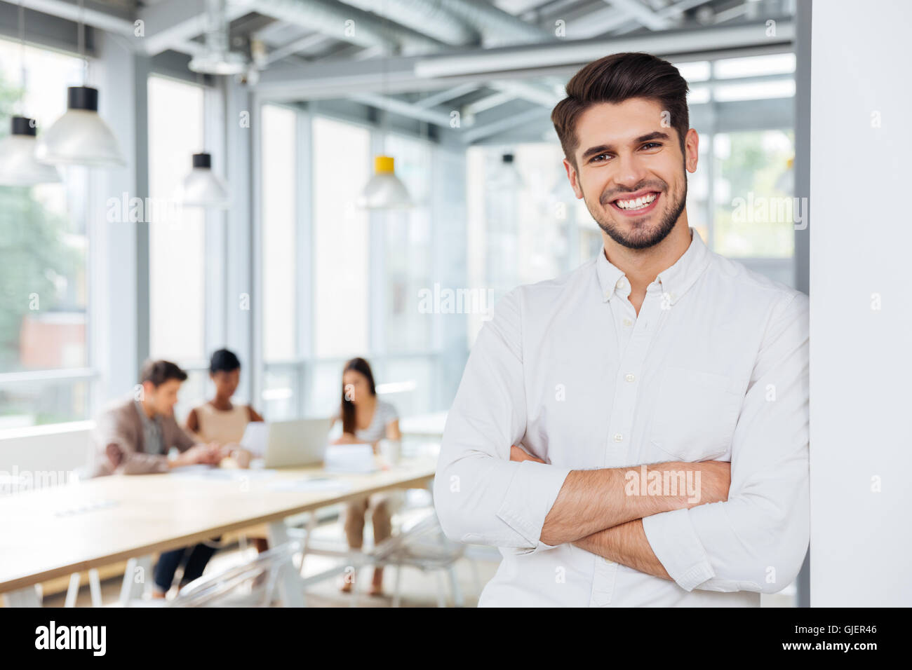 Cheerful handsome young businessman standing with arms crossed in ...