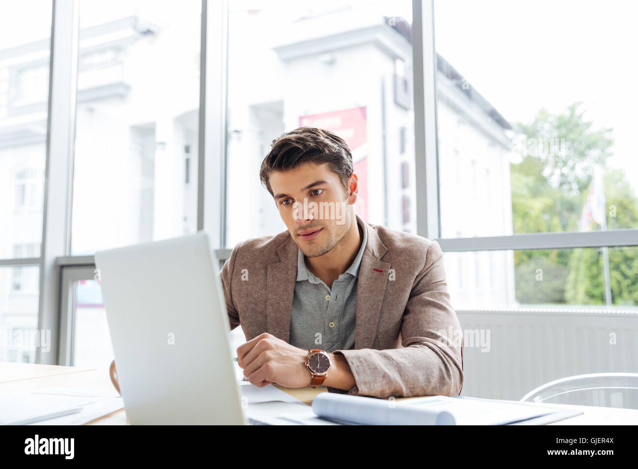 Thoughtful handsome young businessman working with laptop and thinking in office Stock Photo