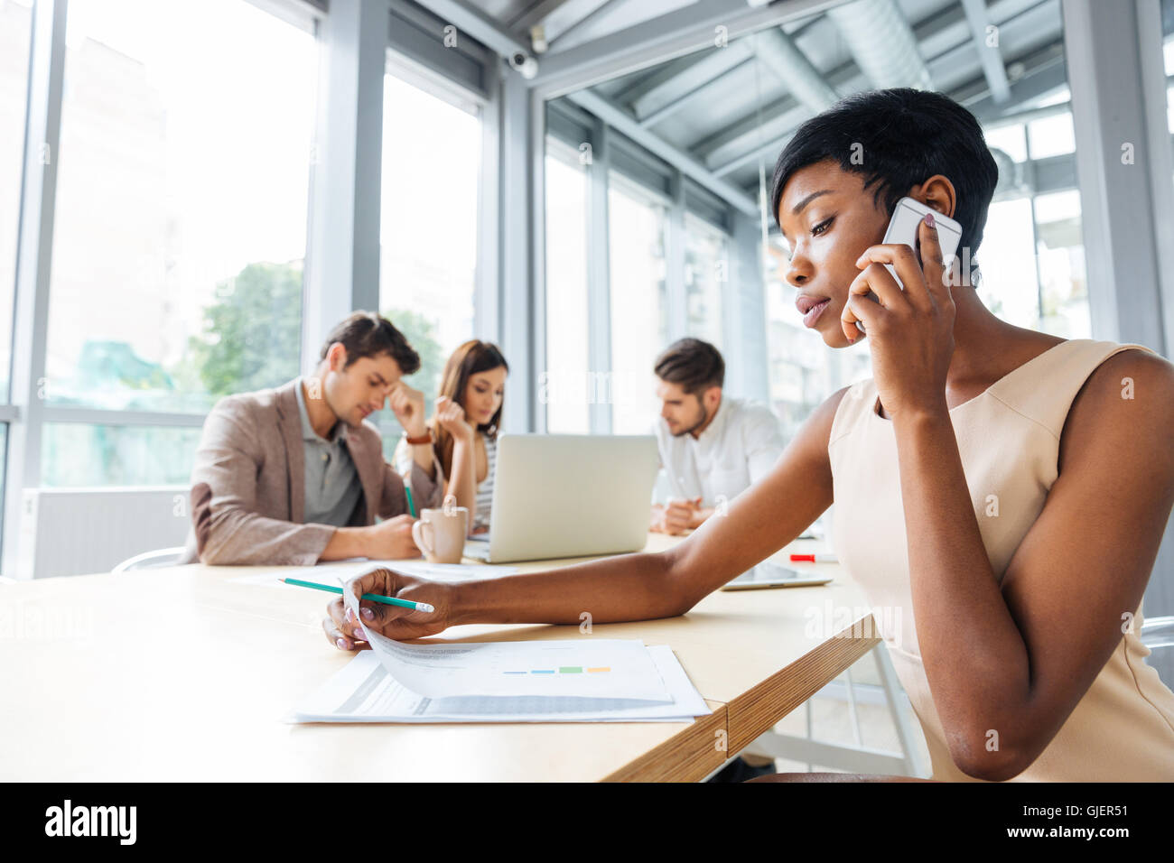 Serious young african businesswoman working and talking on cell phone on business meeting Stock Photo