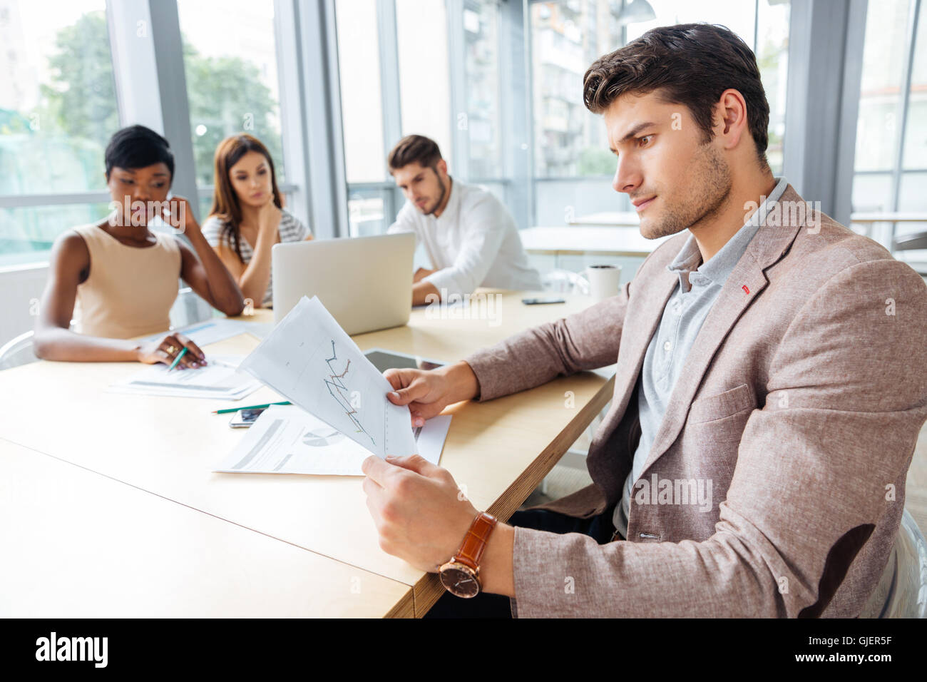 Concentrated young businessman sitting and creating presentation with his business team in office Stock Photo