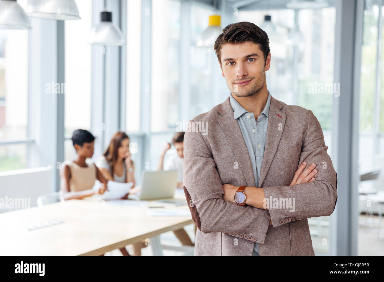 Successful attractive young businessman standing with arms crossed in ...