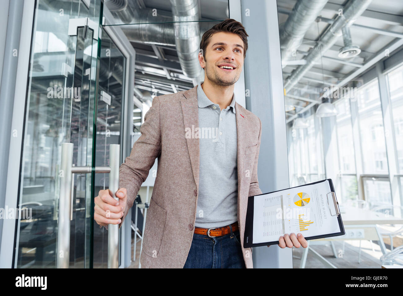 Happy young businessman with business plan on clipboard entering the door in office Stock Photo