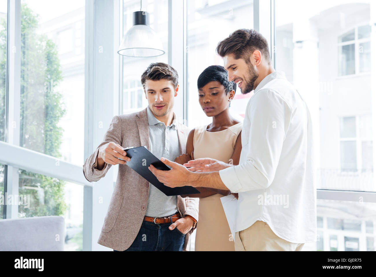 Three young business people standing and discussing business plan together in office Stock Photo
