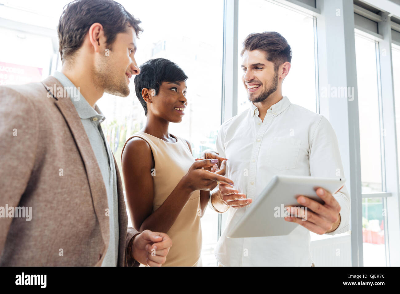 Cheerful young business people talking and using tablet together in office Stock Photo
