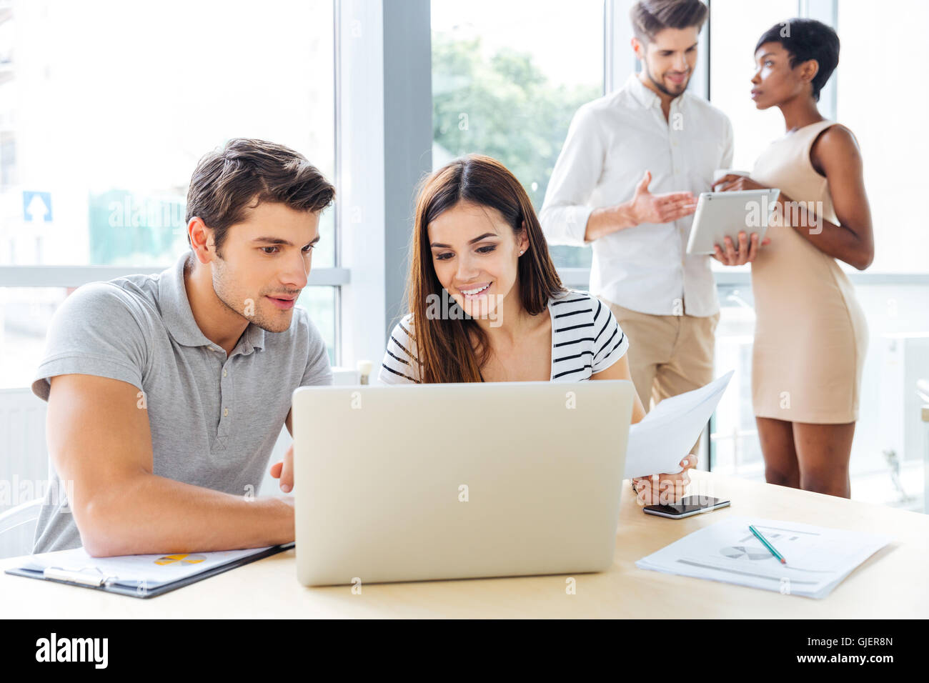 Group of smiling creative young business people working with laptop and tablet in office Stock Photo