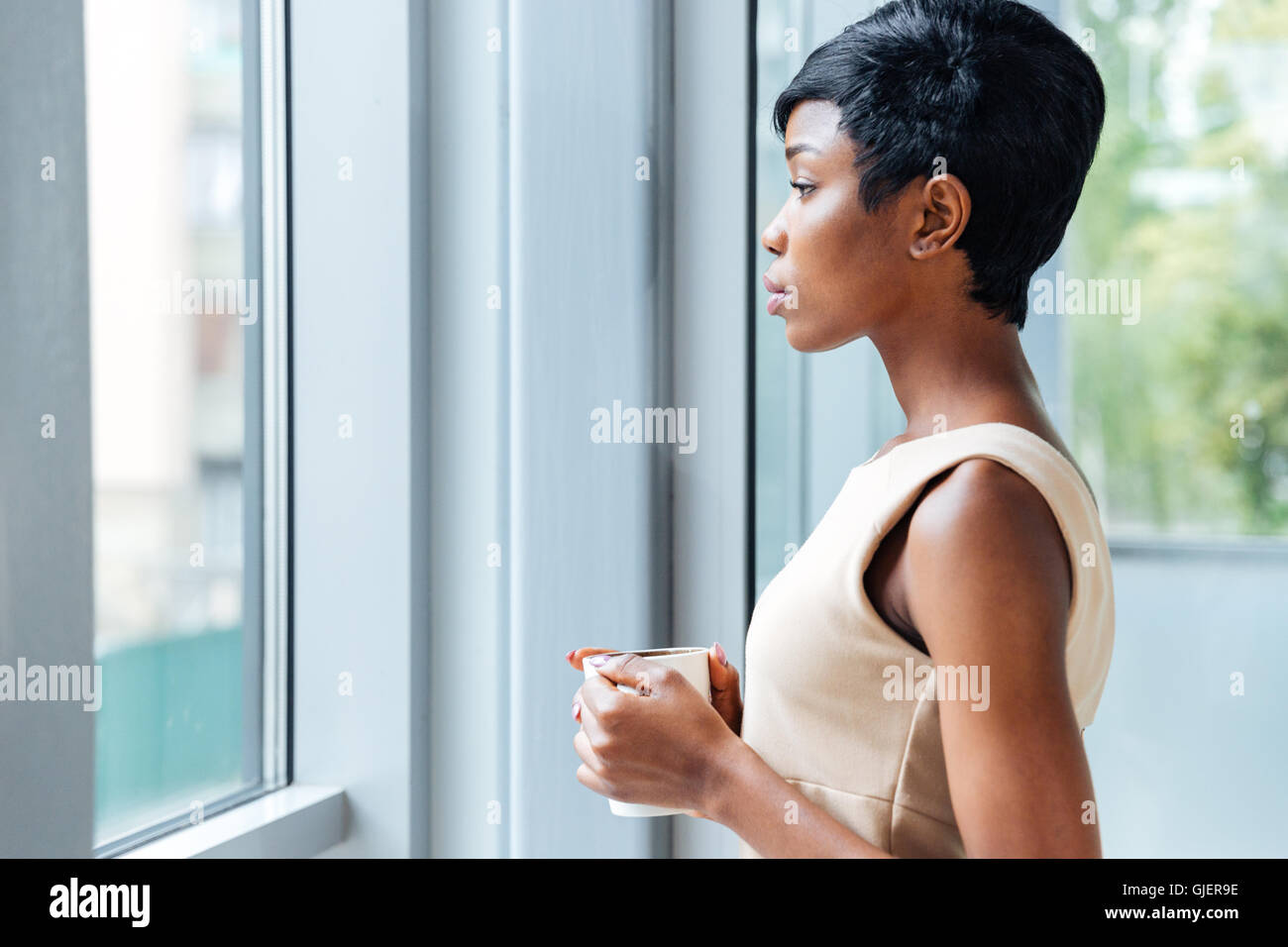 Pensive african american young businesswoman drinking coffee near the window in office Stock Photo