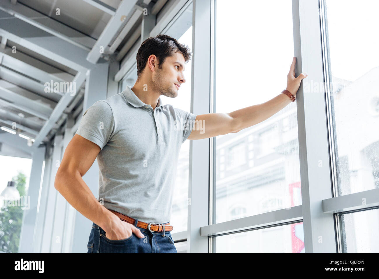 Thoughtful handsome young man standing and looking at the window Stock Photo