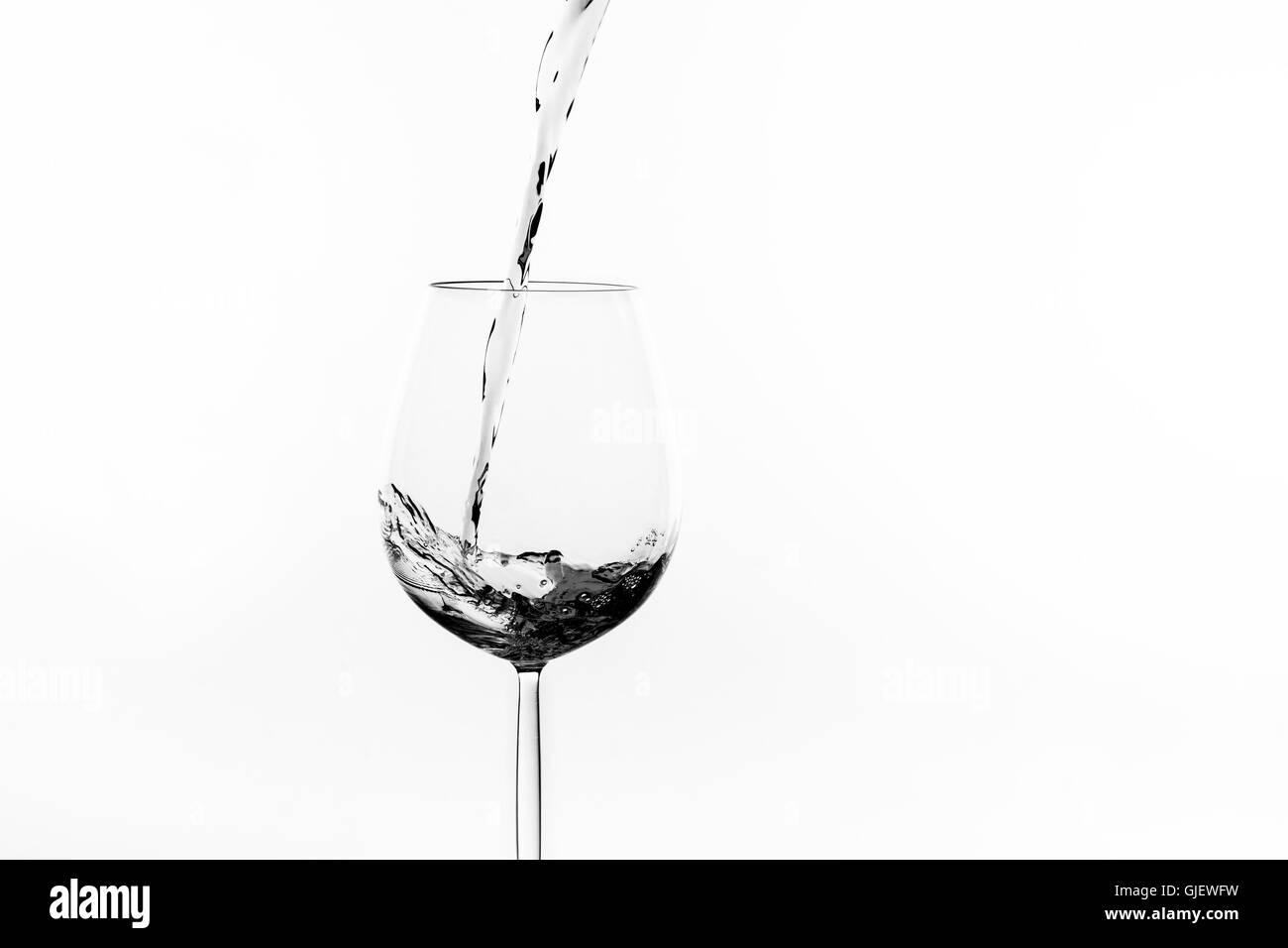 Wine splashes into a wine glass in black and white Stock Photo