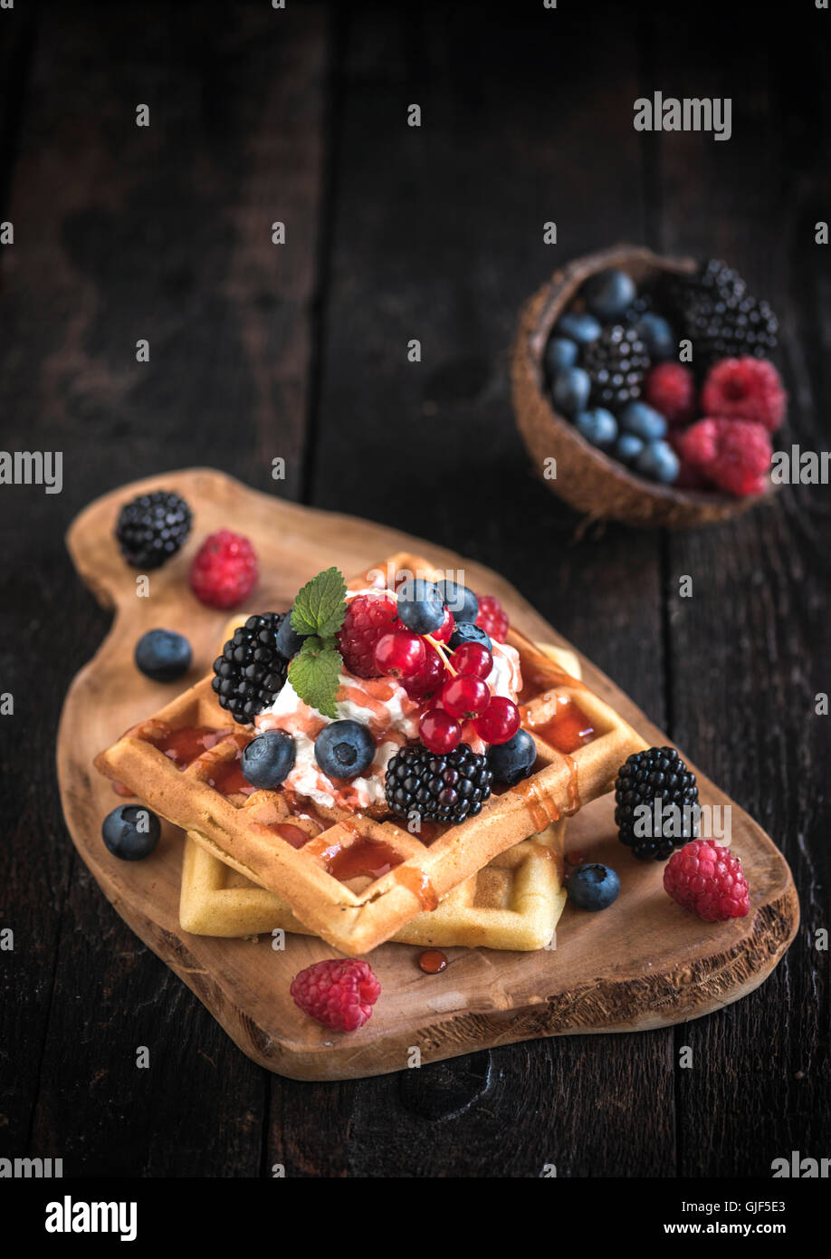 Belgium waffles with berry fruits and ice cream on top on wooden board ...