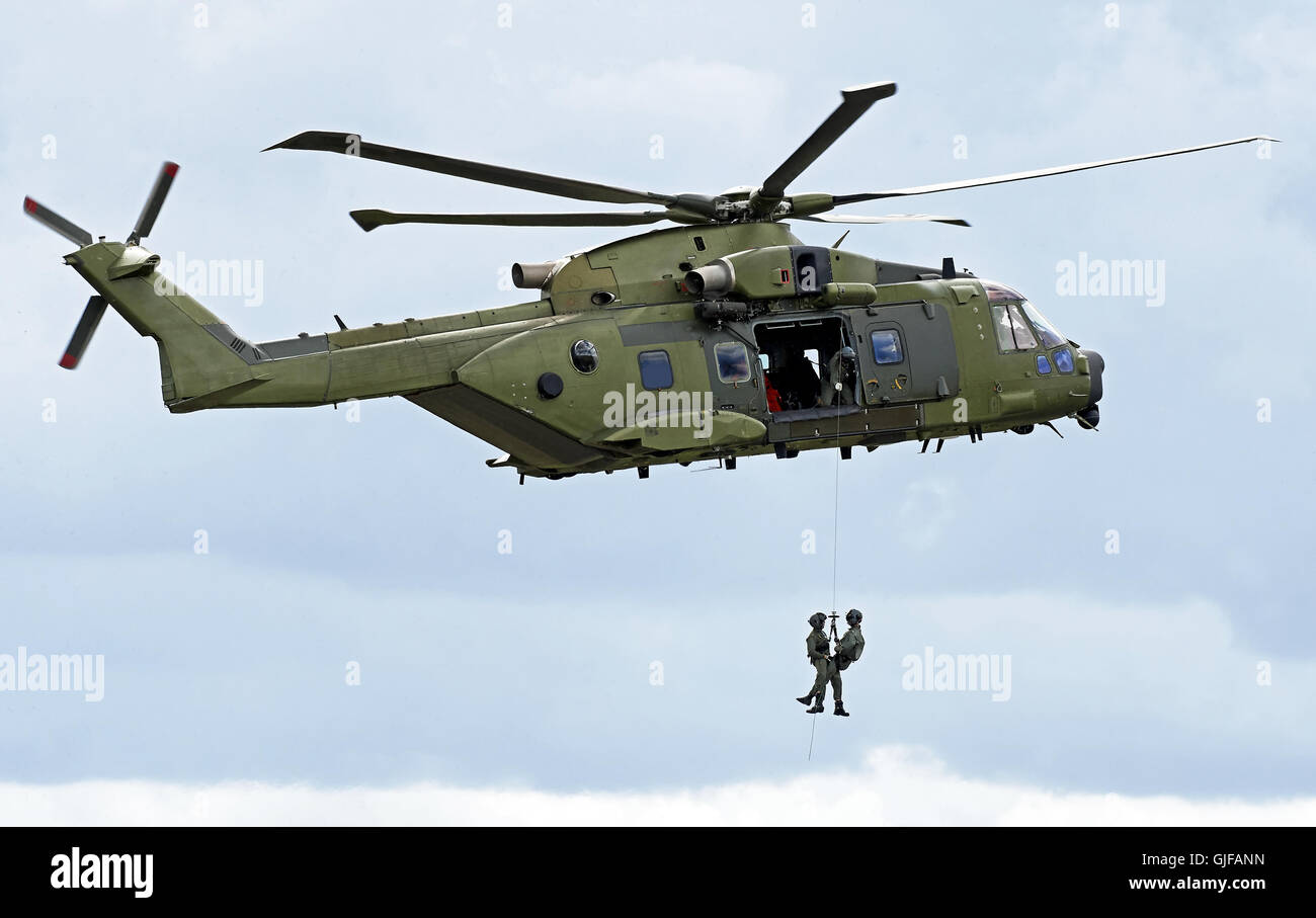 Military rescue helicopter hoisting personnel with clouds in the background Stock Photo