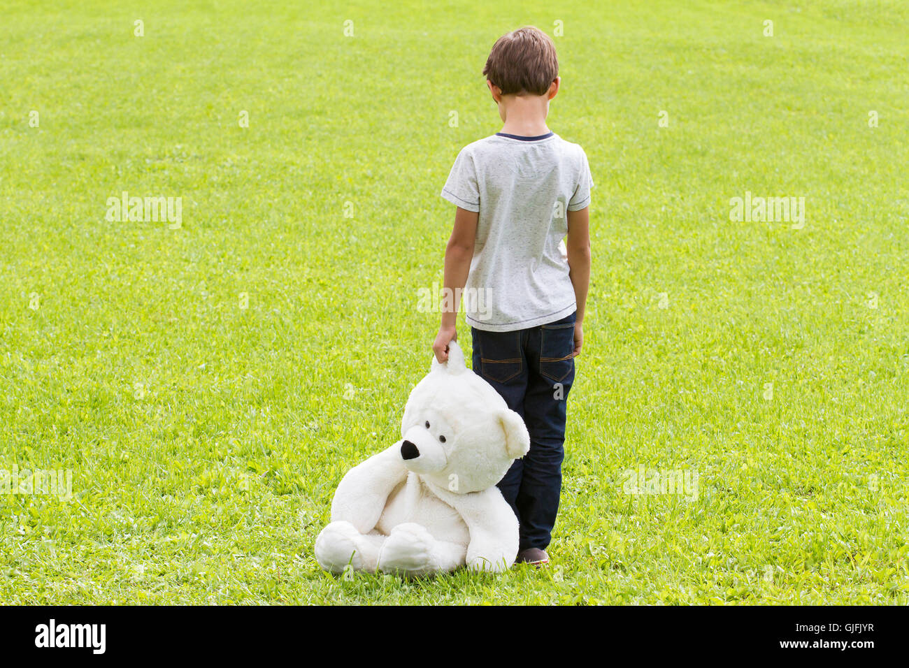 Sad young boy is holding a teddy bear and standing on the meadow. Child ...