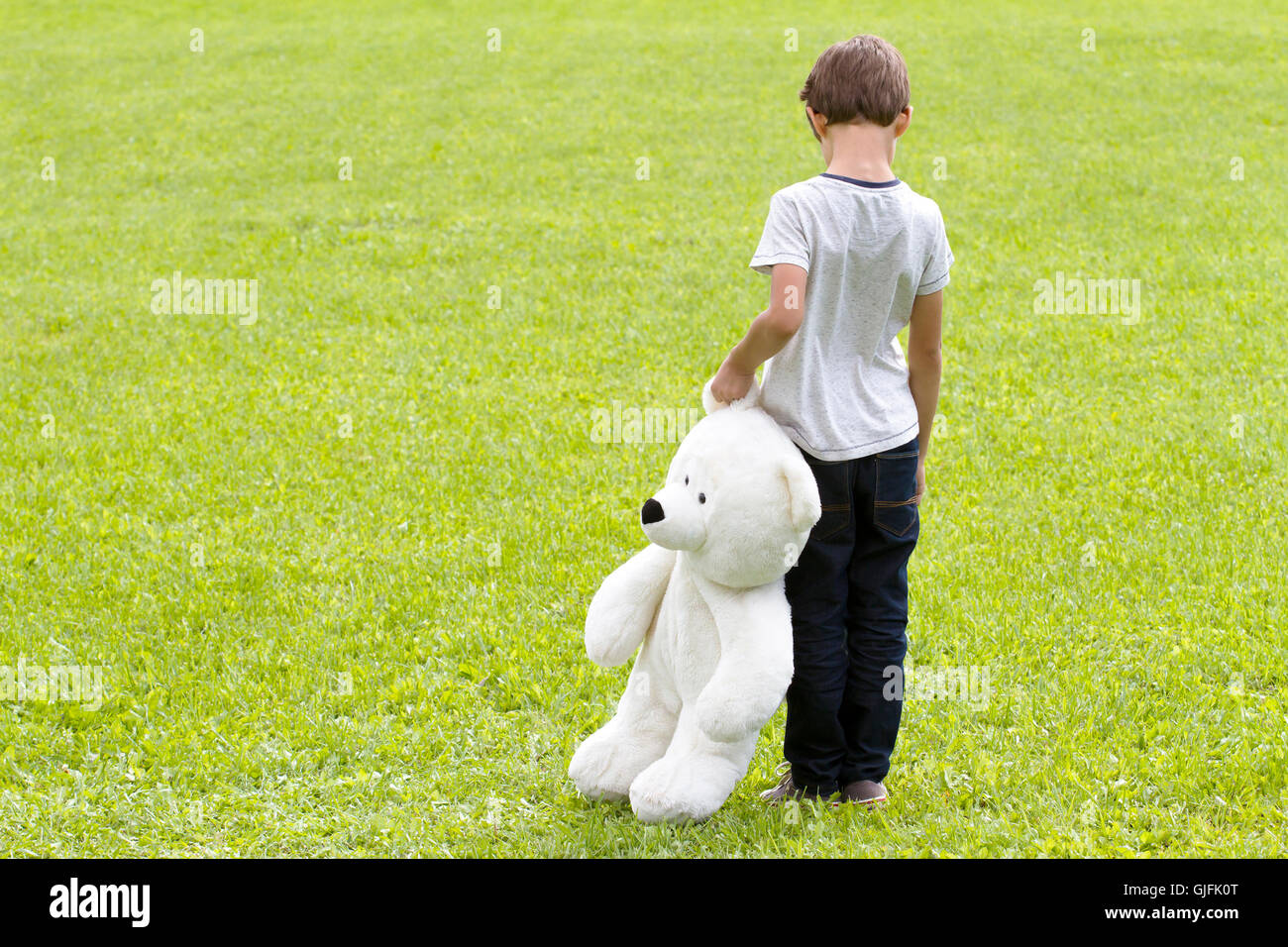Sad young boy is holding a teddy bear and standing on the meadow. Child ...