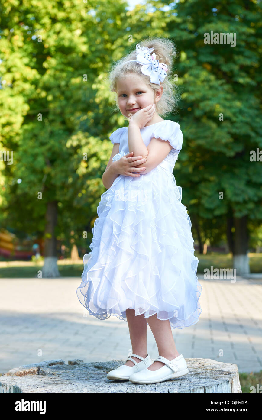 child girl in white gown posing, happy childhood concept, summer season in city park Stock Photo