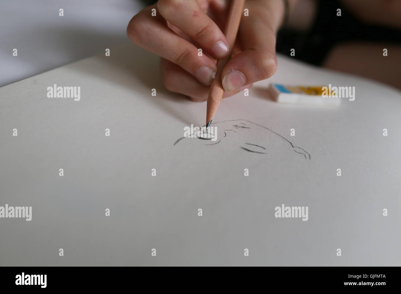 A girls hand holding a pencil and drawing a face, Manga style on white paper. Stock Photo